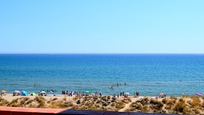 A beach with people, tents, and umbrellas. - Frontline apartment with garden and pool. Parking . Capacity 4 Persons. WIFI (PALS)