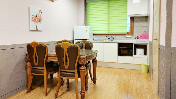 A dining area with a wooden table and chairs, a refrigerator, a microwave, and a window with blinds. - Haegil House (Jeju City)