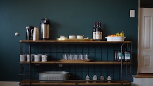A metal cart with shelves holding mugs, a kettle, wine bottles, and fruit. - Spoke and Vine Motel (Palisade)