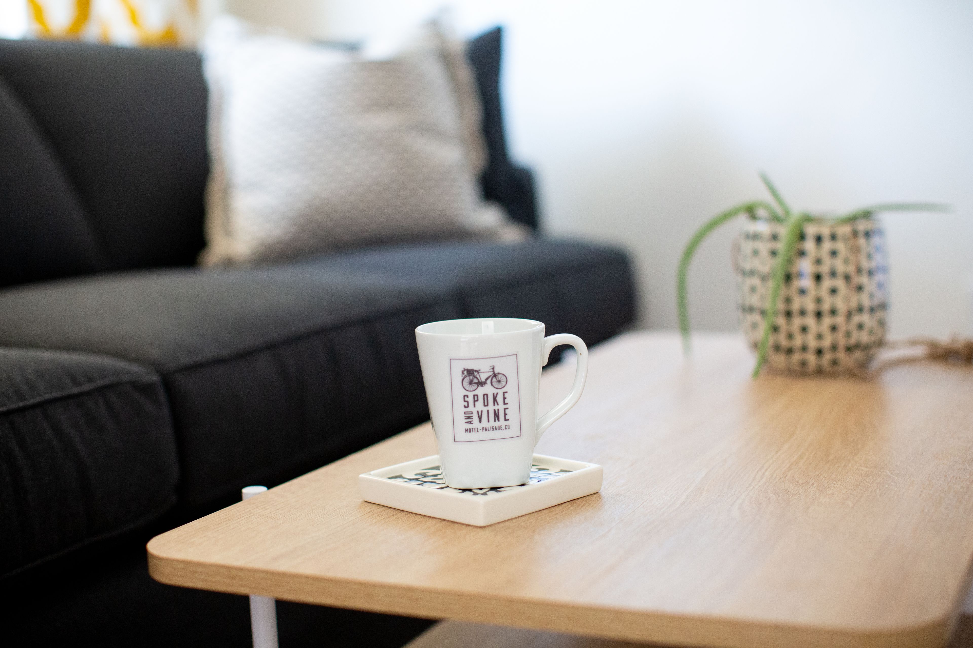 Una taza blanca con el logo de una bicicleta sobre un posavasos en una mesa de madera.