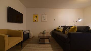 A living room with a sofa, a coffee table, and a TV mounted on the wall.