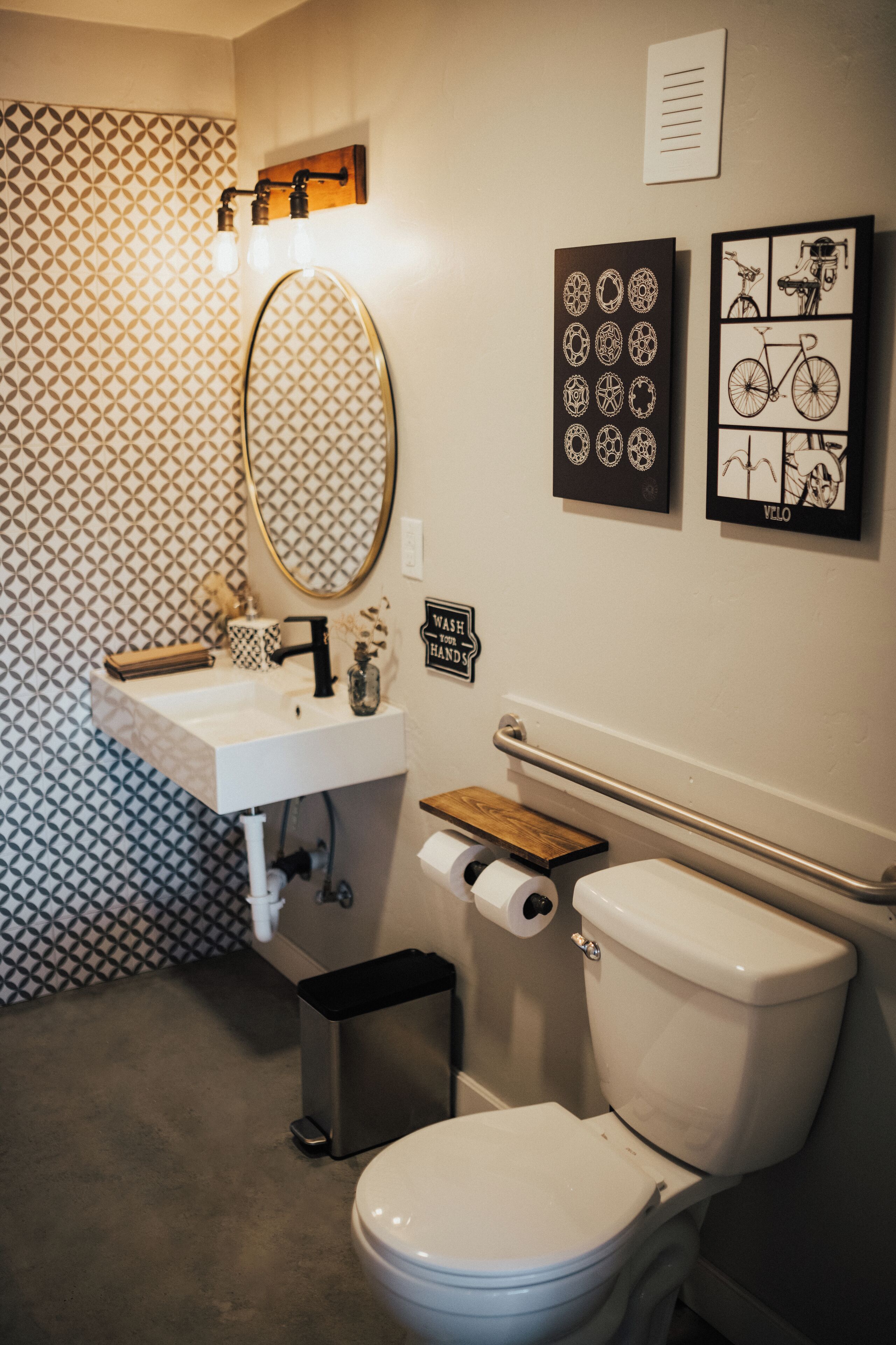 A bathroom with a white sink, mirror, toilet, and patterned wallpaper.