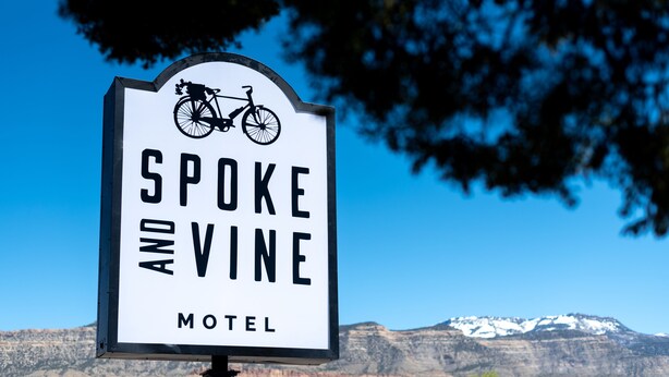 A sign for the Spoke and Vine Motel with a bicycle symbol, set against a mountainous backdrop. - Spoke and Vine Motel (Palisade)