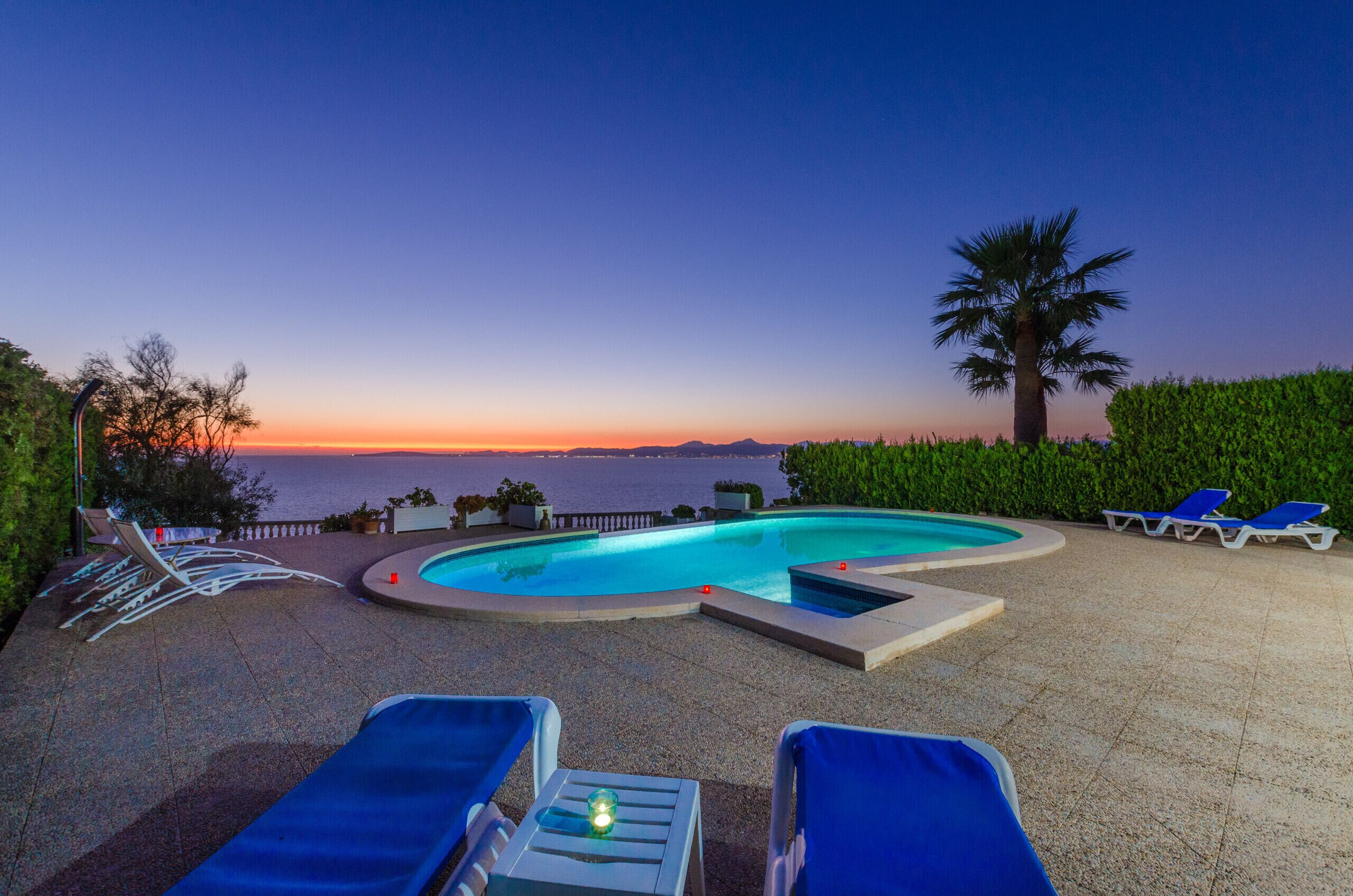 Zona de piscina con sillones de descanso y vista al mar al atardecer.