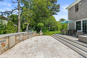A patio with stone flooring, outdoor furniture, and a grill area.