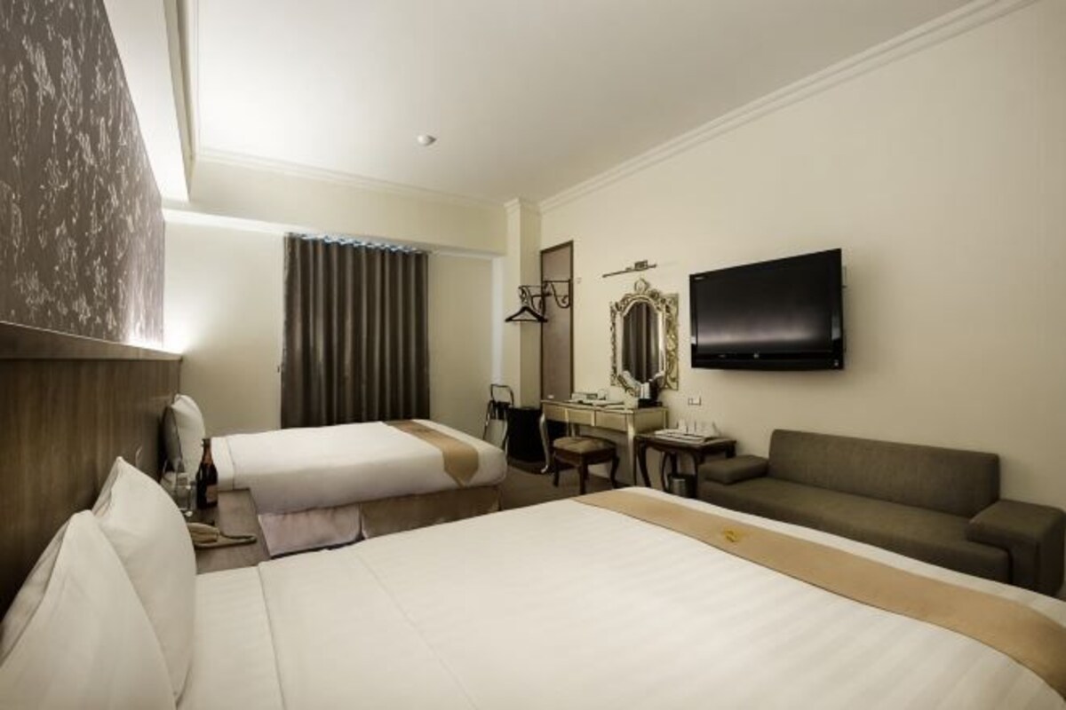 A hotel room with two beds, a desk, a chair, a television, and a mirror.