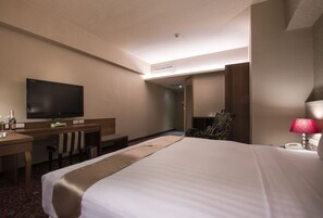 A hotel room with a bed, a desk with a flat-screen TV, a chair, a lamp, and a minibar. - Hu house (Kaohsiung)