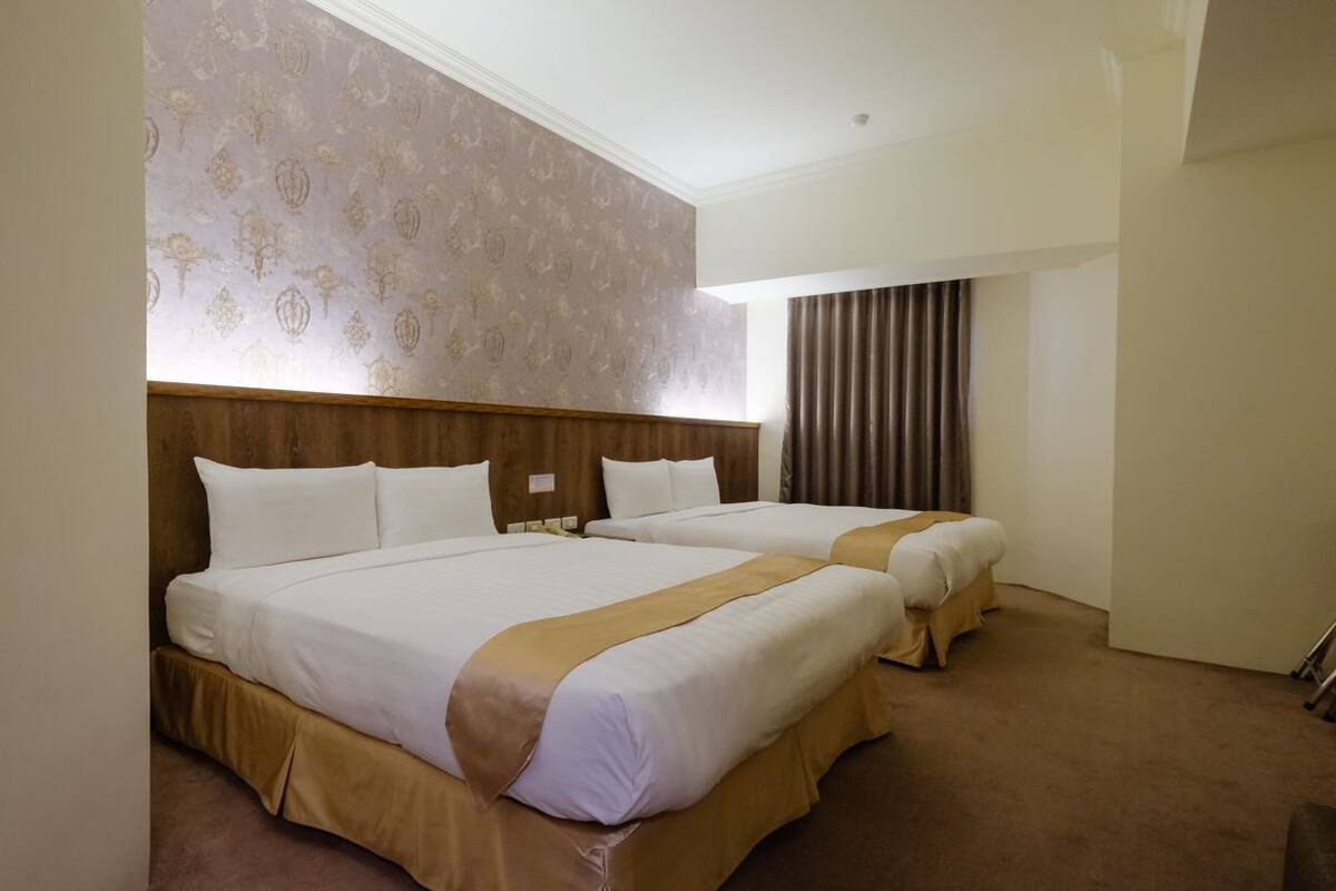 A hotel room with two beds, a wooden headboard, a patterned wallpaper, and a curtain.