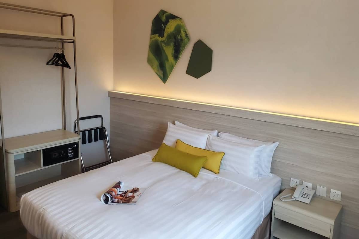 A hotel room with a bed, a bedside table with a phone, a lamp, and a coat rack.