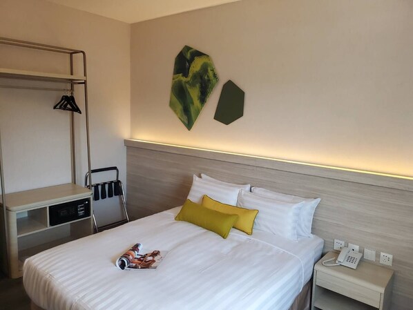 Una habitación de hotel con una cama, una mesita de noche con un teléfono, una lámpara y un perchero.
