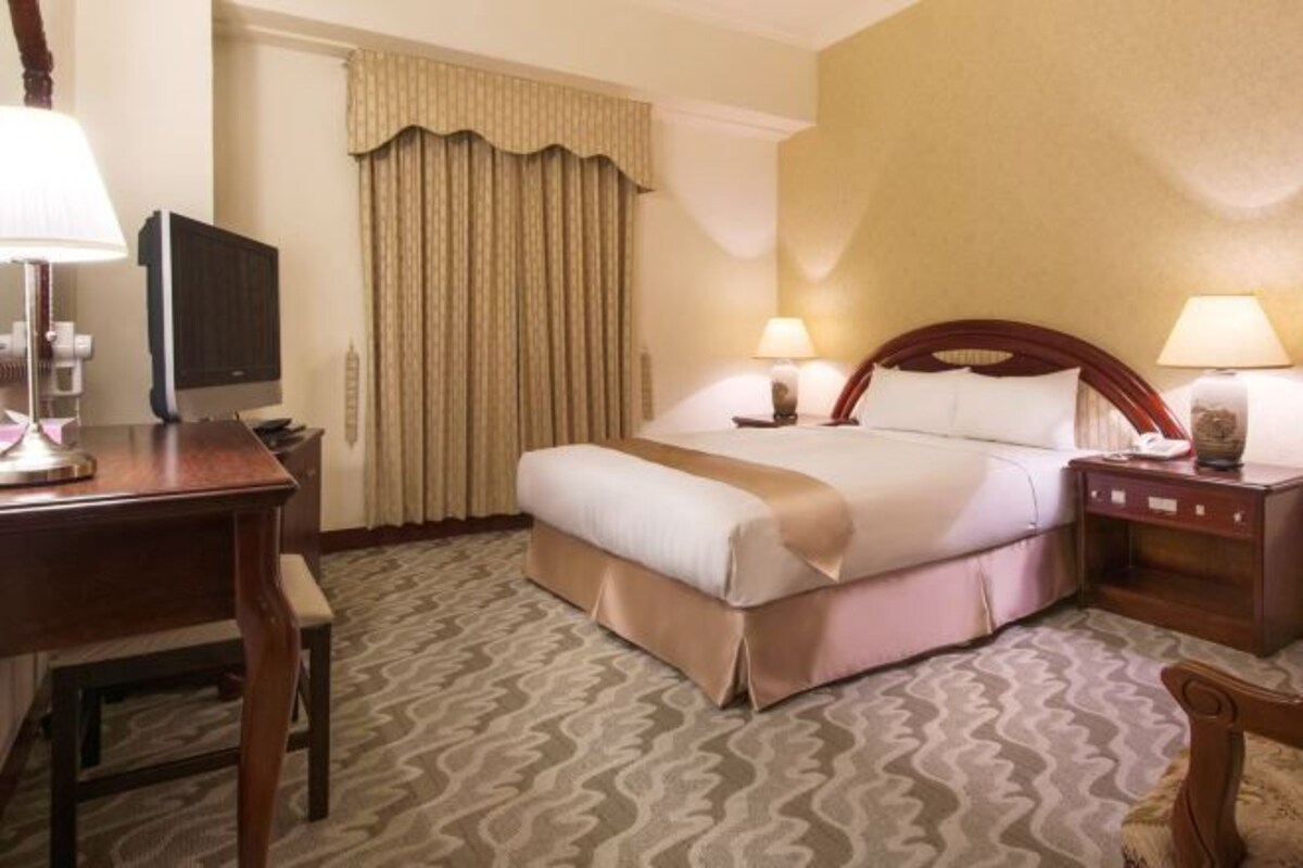A hotel room with a bed, bedside lamps, a television, a desk, and a chair.
