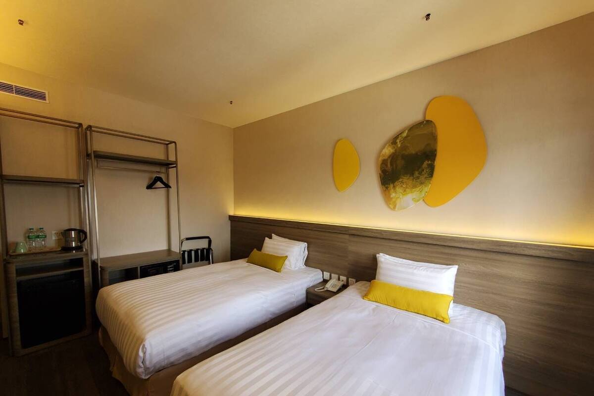 A hotel room with two beds, a desk with a chair, a coat rack, and a wall-mounted phone.