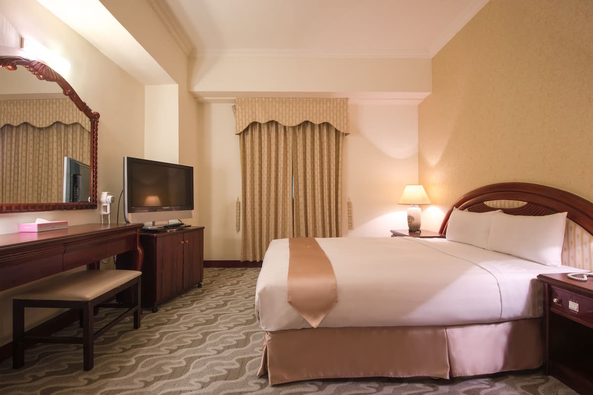 A hotel room with a bed, a desk with a television, a lamp, and a mirror.
