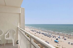 A balcony with a view of a beach, white plastic chairs, and a white railing. - Oceanfront Penthouse in Paradise w Indoor Pool (North Myrtle Beach)