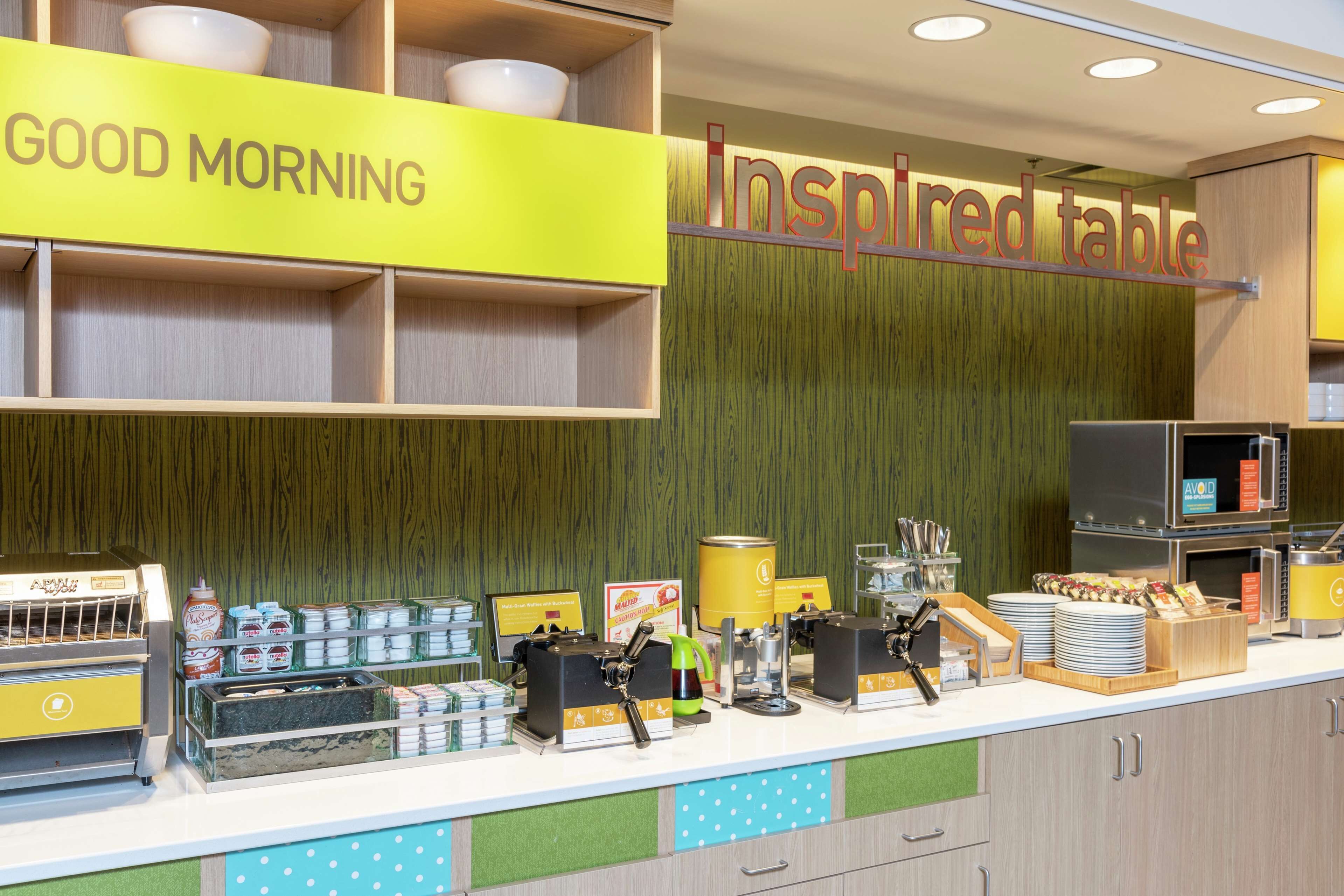 A breakfast counter with a 'GOOD MORNING' sign, a 'Inspired table' sign, and various breakfast items and equipment.