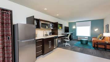 Una cocina moderna con refrigerador, microondas y lavavajillas, una zona de comedor con mesa y sillas, y una sala de estar con sofá y lámpara.