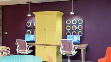 Une pièce comprenant deux bureaux, chacun équipé d’un ordinateur et d’une chaise, un meuble jaune et des œuvres d’art accrochées au mur.