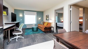 Habitación de hotel con escritorio, silla de oficina, sofá y mesa de comedor.