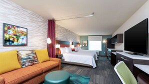 Habitación de hotel con sofá, dos camas, escritorio, televisión y un cuadro en la pared.