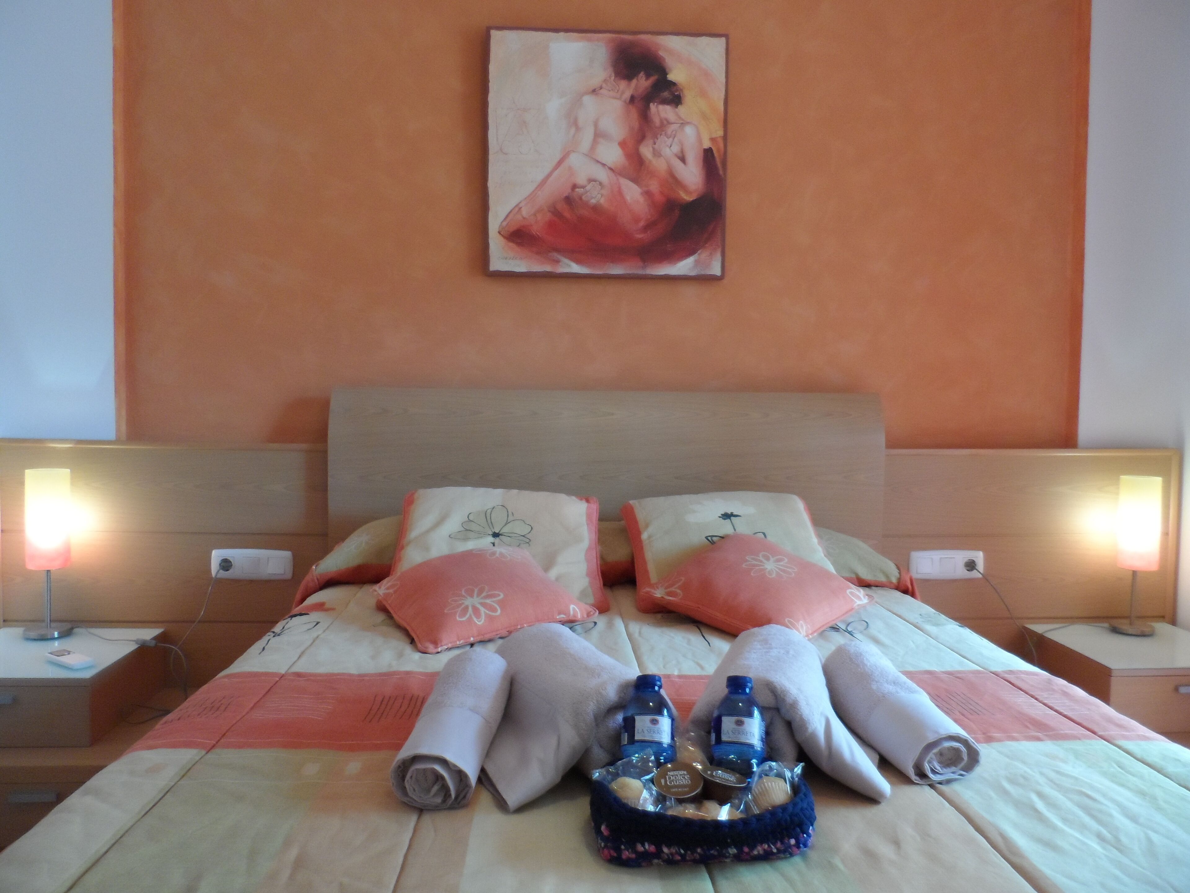 A neatly made bed with towels, a tray of toiletries, and a painting on the wall.