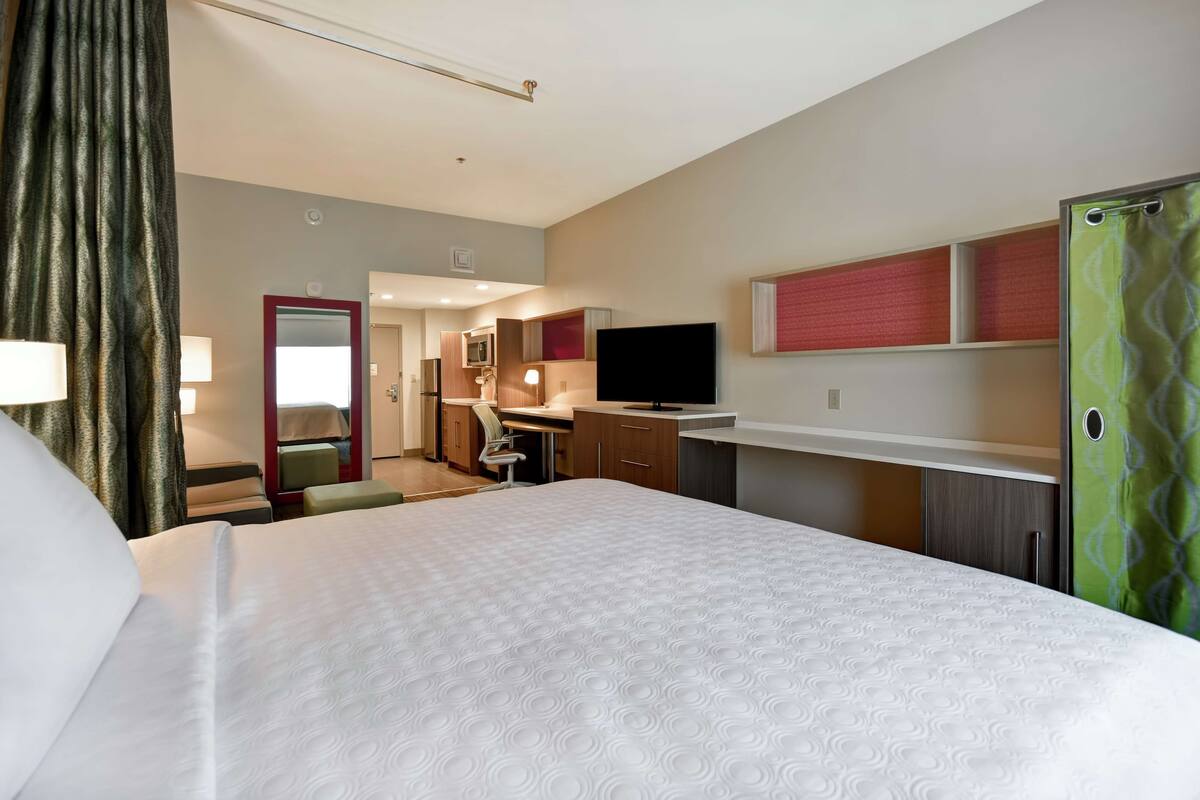 Une chambre d’hôtel avec un grand lit, un bureau avec une chaise, une télévision et une armoire.