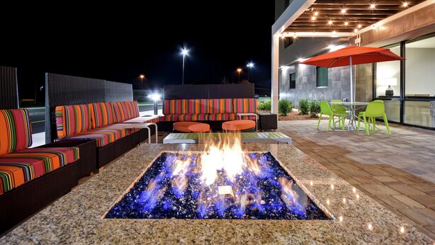 An outdoor seating area with a fire feature, green chairs, and a modern building in the background. - Home2 Suites by Hilton Birmingham Fultondale (Fultondale)
