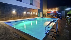 An outdoor swimming pool with a metal ladder, surrounded by stone walls and illuminated by ambient lighting. - Home2 Suites by Hilton Birmingham Fultondale (Fultondale)