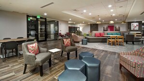 A modern hotel lobby with a seating area, a conference room, and a reception desk. - Home2 Suites by Hilton Birmingham Fultondale (Fultondale)