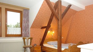 Une chambre avec un plafond en pente, un lit en bois, une table de chevet, une chaise et une fenêtre avec des rideaux.