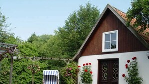 Une maison traditionnelle en bois, avec une façade blanche, une porte marron foncé et une petite fenêtre.