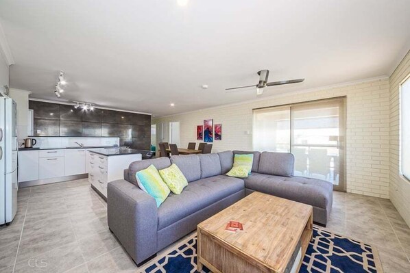 A modern living room with a grey sectional sofa, a wooden coffee table, and a kitchen in the background. - One of a Kind Beach Front Unit (WOORIM)