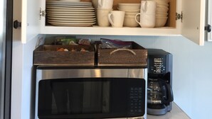 Cozinha com micro-ondas e cafeteira na bancada, e armário acima com pratos e xícaras empilhados.