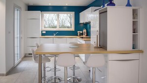 A modern kitchen with white cabinets, a wooden countertop, and a window. There are three white bar stools and a sink. - 3 bedroom awesome home in Matignon (Matignon)