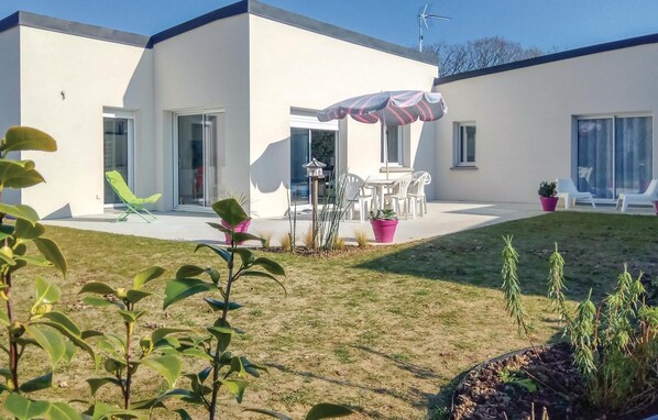 A modern house with a patio, a table with chairs, and a large umbrella.