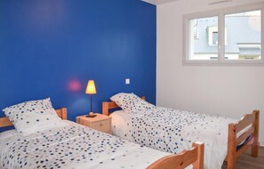 A bedroom with two single beds, a nightstand with a lamp, and a window with a view of a building.