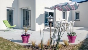 A modern outdoor patio with a green lounge chair, a table with white chairs, and two potted plants. - 3 bedroom awesome home in Matignon (Matignon)