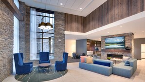 A spacious living area with stone walls, a large TV, and a fireplace. - Hyatt Place Anchorage Midtown (Anchorage)