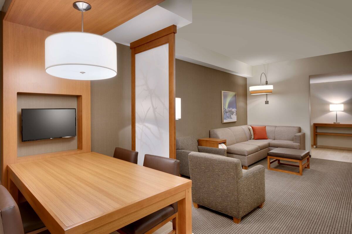 Una habitación de hotel moderna con una mesa de comedor de madera, un televisor de pantalla plana, un sofá y un sillón pequeño.