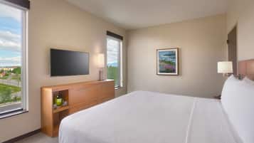 A hotel room with a bed, a TV, a desk, and a window with a view of the city.