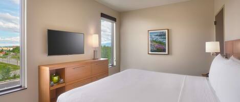 Quarto de hotel com cama, televisão, secretária e janela com vista para a cidade.