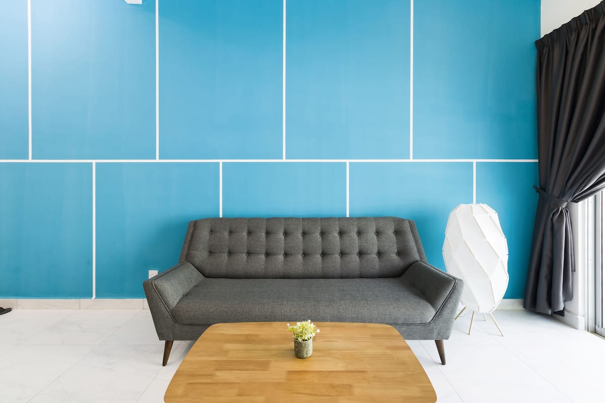Un salon moderne avec un canapé gris, une table basse en bois agrémentée d’une petite plante et un objet décoratif blanc placé contre un mur bleu.