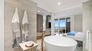 Un baño moderno con una bañera grande, una mesita de noche con artículos de aseo y toallas colgadas en un perchero.