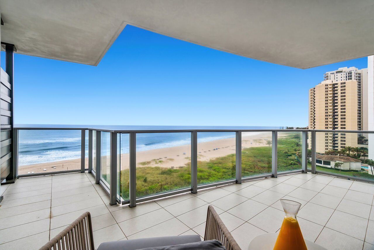 A balcony with a view of the beach and ocean, featuring a table and chairs.