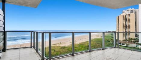 A balcony with a view of the beach and ocean, featuring a table and chairs.