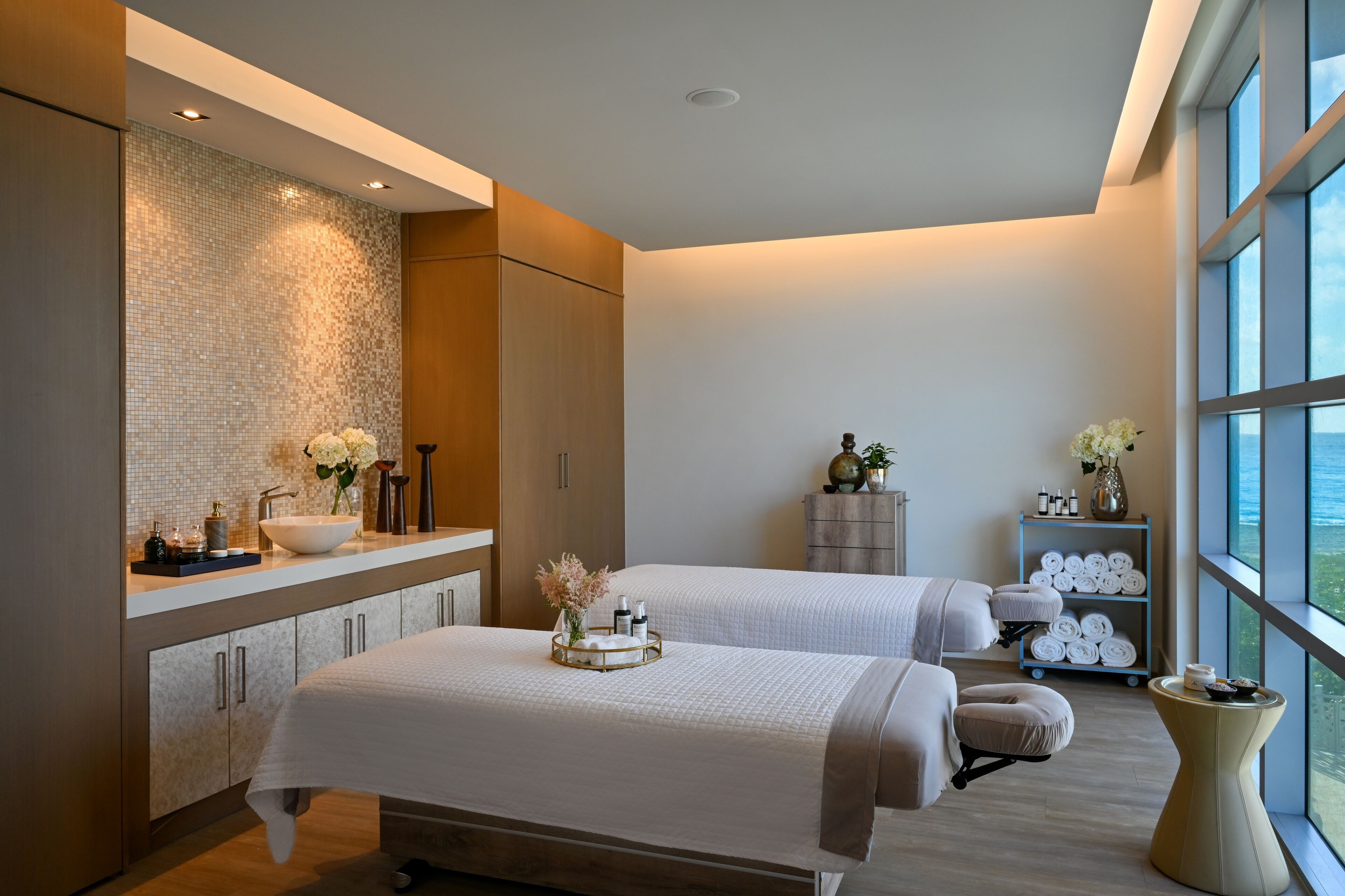 A modern spa room with two beds, a large window, and a view of the city.