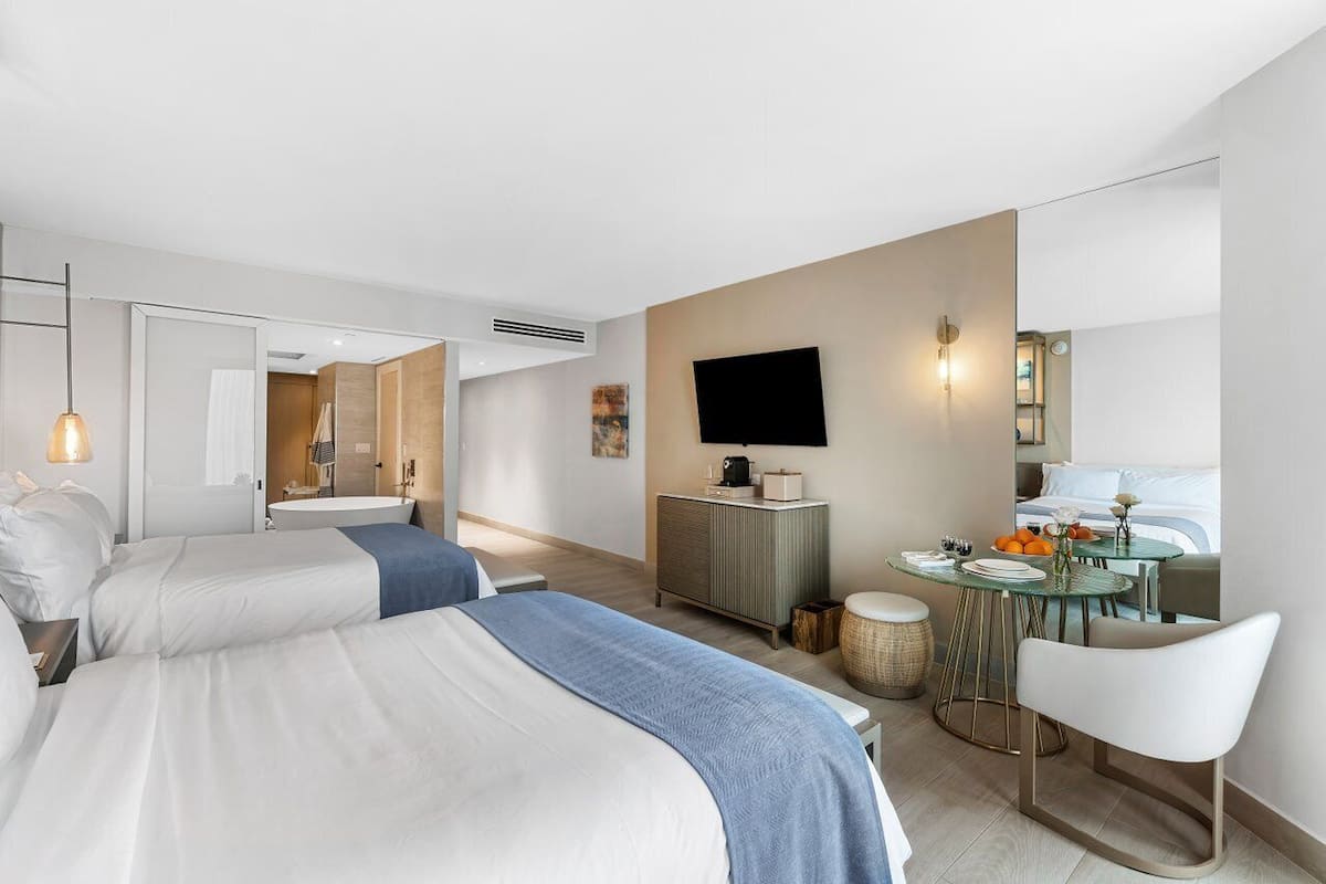 A modern hotel room with a large bed, a desk with a chair, a television, and a bathroom visible through an open door.
