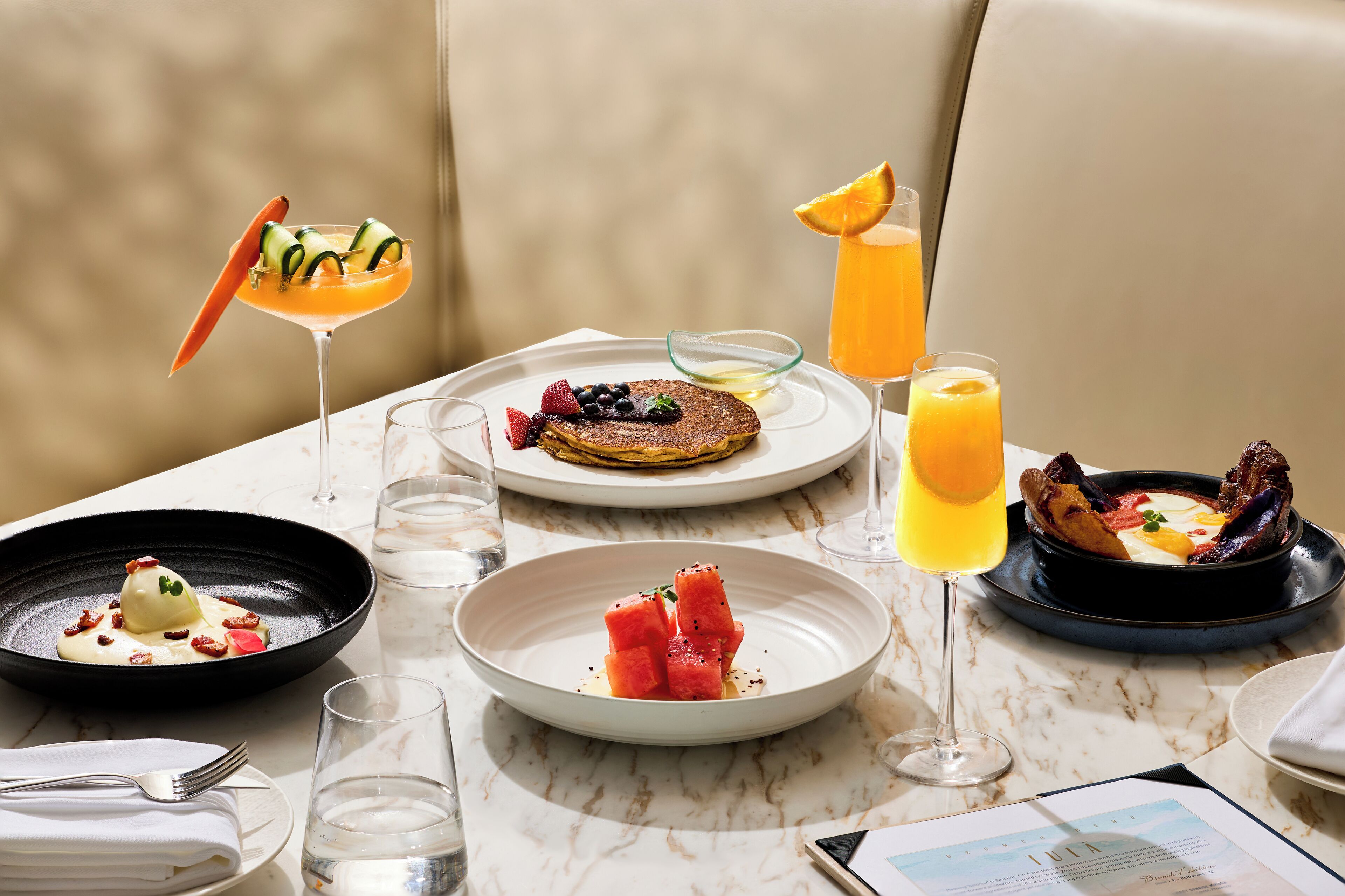 Un desayuno con diferentes platos, bebidas y un menú sobre una mesa de mármol.