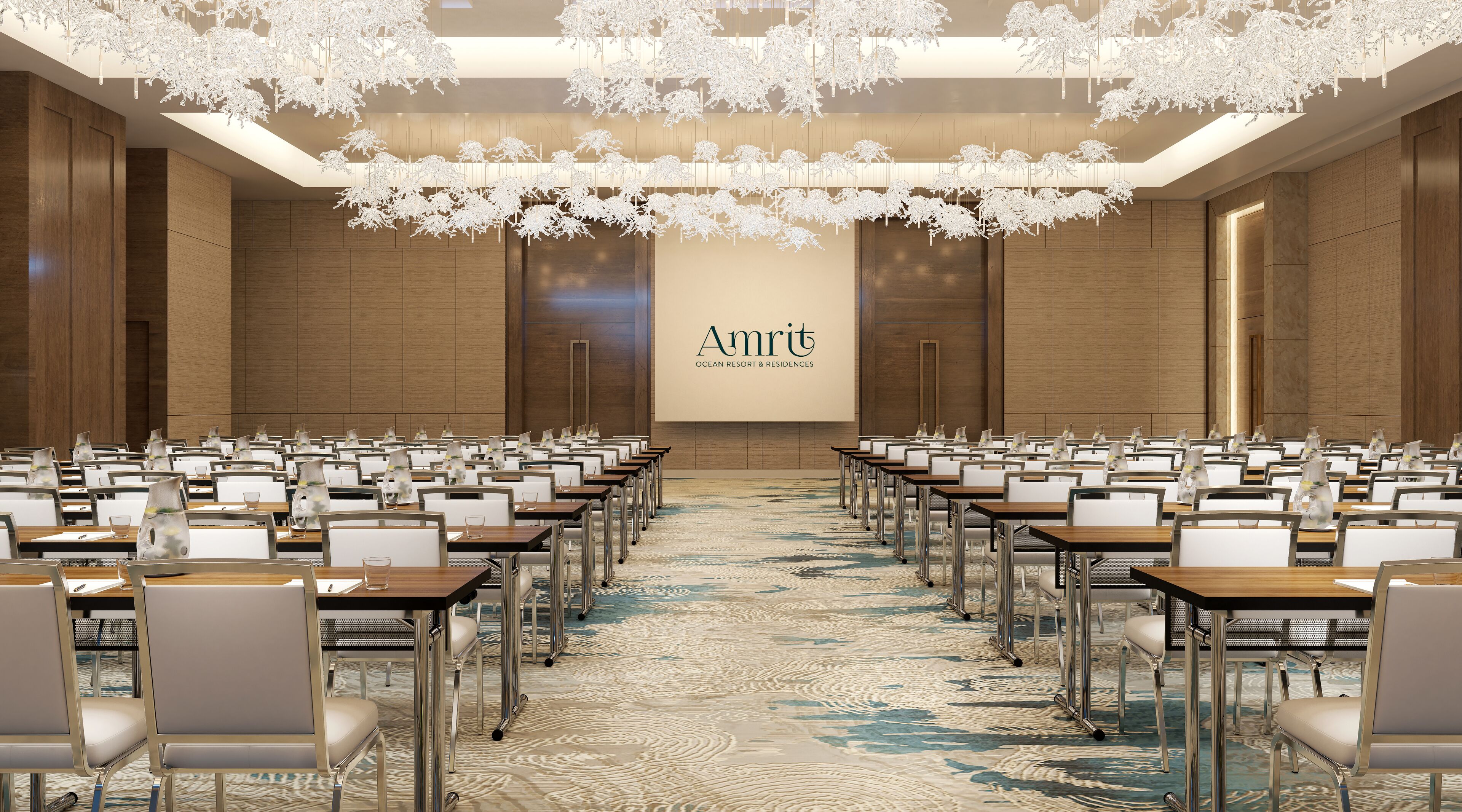 A conference room with rows of tables and chairs, a large screen displaying 'Amrit Ocean Resort & Residences', and a patterned carpet.