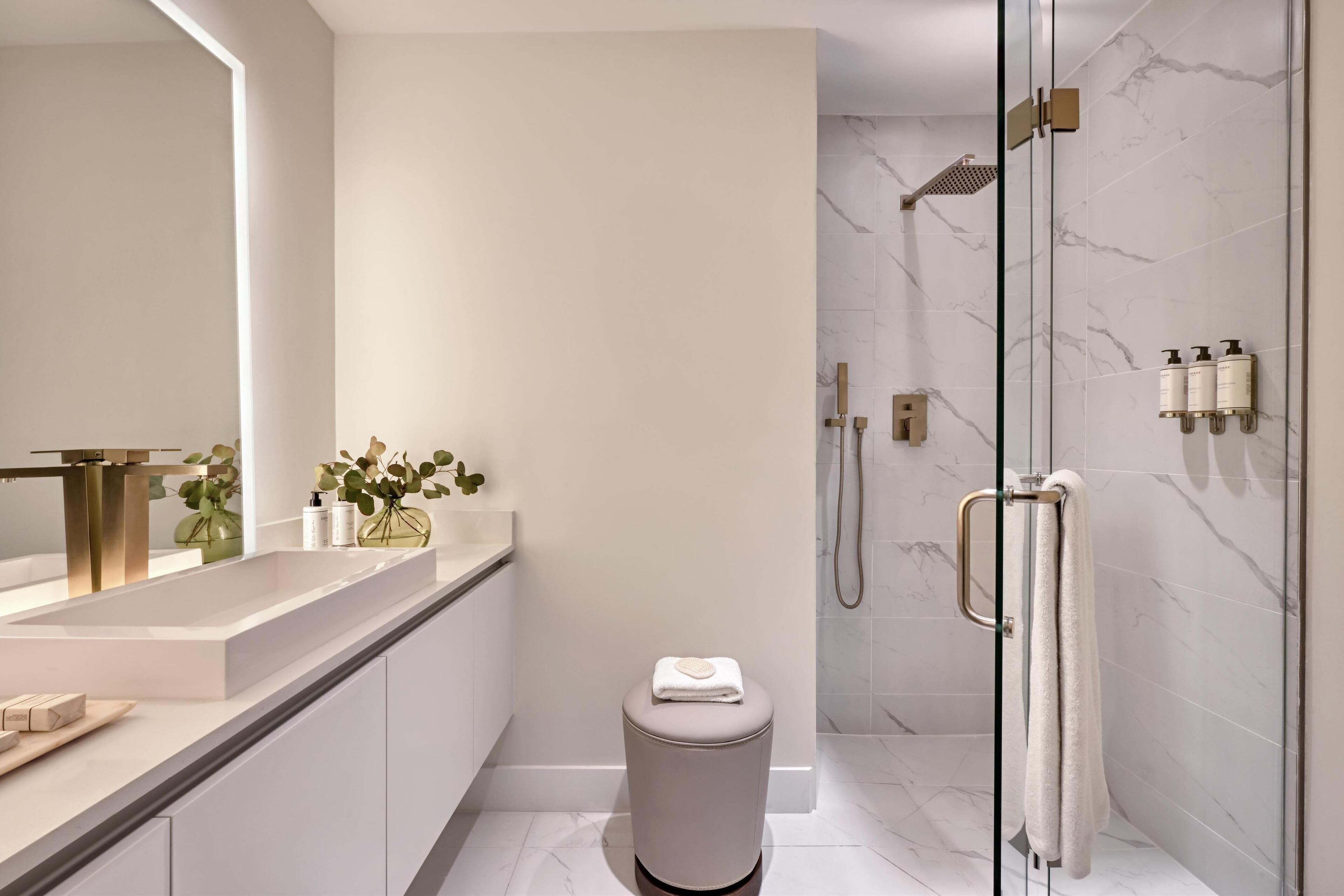 A modern bathroom with a glass-enclosed shower, a vanity with a gold sink, and a small trash bin.