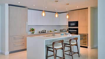 A modern kitchen with a central island, bar stools, pendant lighting, and built-in appliances.
